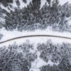 a road through a snowy winter forest viewed from above